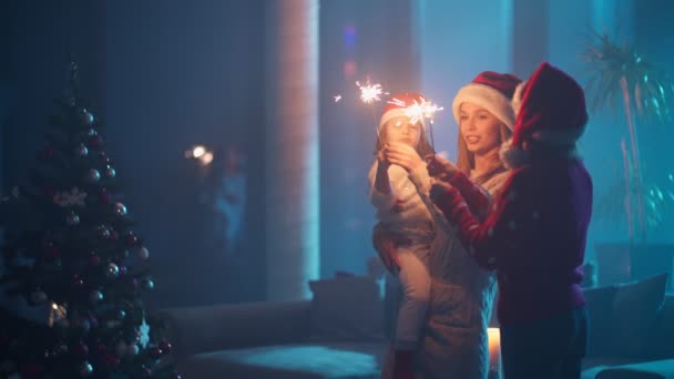 Madre e le sue figlie utilizzando scintille vicino all'albero di Natale — Video Stock