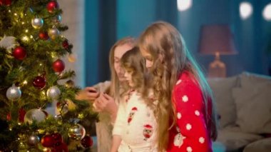 Küçük kızlar annelerine Noel ağacı süslemesinde yardım ediyor.