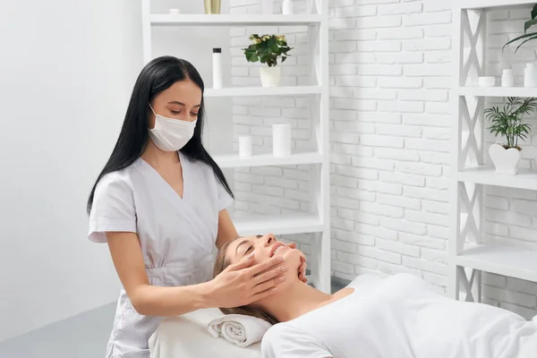 Esteticista en máscara protectora haciendo masaje cara. — Foto de Stock