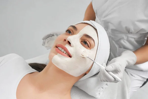 Schoonheidsspecialiste doet masker gezicht procedure voor jonge vrouw. — Stockfoto