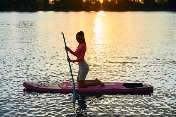 Ajuste jovem surfando na prancha de remo durante o pôr do sol — Fotografia de Stock