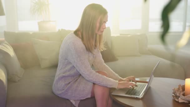 Mujer sentada en el sofá y escribiendo en el portátil inalámbrico — Vídeos de Stock