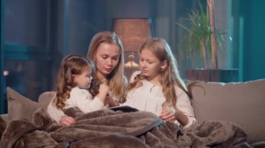 Anne ve kızları kanepede oturup resim yapıyorlar.