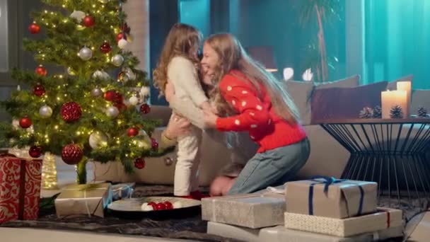 Moeder zitten in de buurt van kerstboom en knuffelen haar dochters — Stockvideo