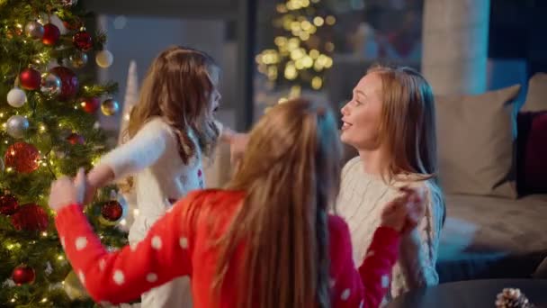 Két vidám lány játszik anyával a karácsonyfa mellett. — Stock videók