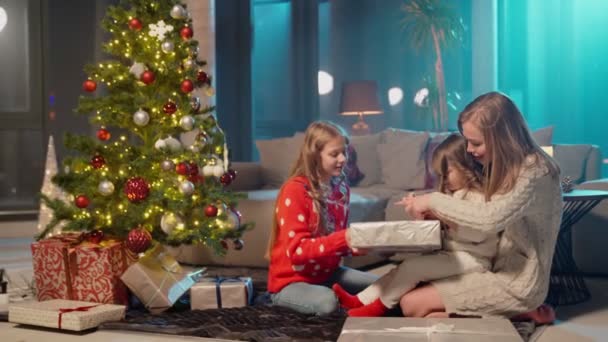 Vidám lányok és az anyjuk karácsonyi ajándékokat nyitnak. — Stock videók