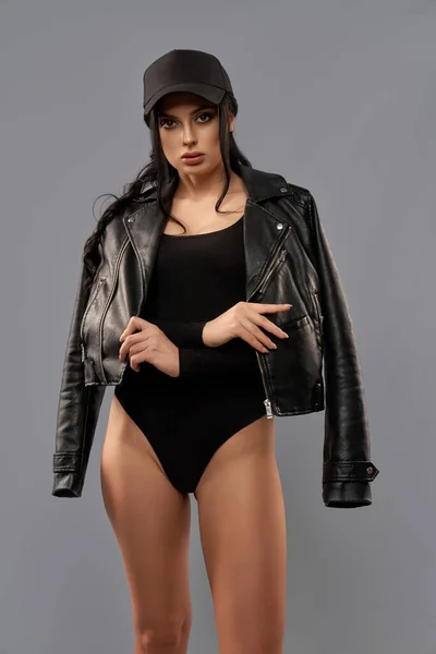 Mulher de bodysuit preto, boné e jaqueta de couro em estúdio — Fotografia de Stock