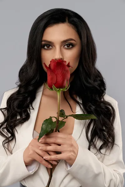 Frau versteckt Lippen hinter roter Rose vor grauem Hintergrund — Stockfoto