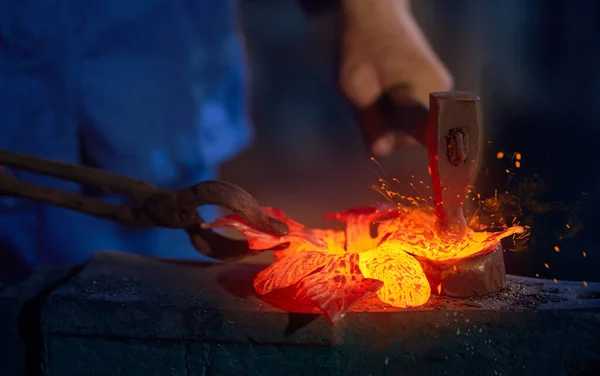 Pracovník v modré uniformě vyrábějící kov s ohněm v kovárně. — Stock fotografie