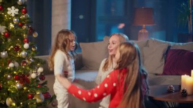 Anne ve kızları Noel ağacının yanında şarkı söylüyorlar.