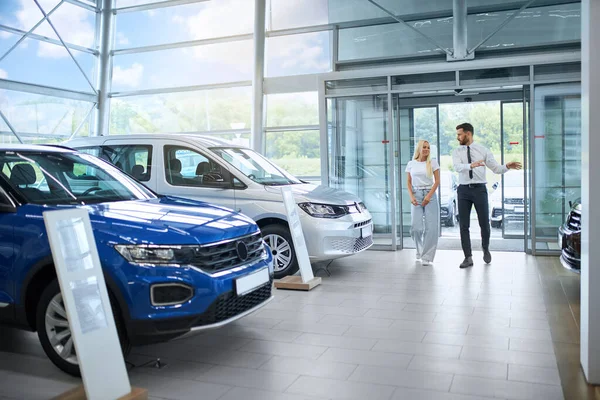 Salesman showing various cars to female client at shop — Stock fotografie