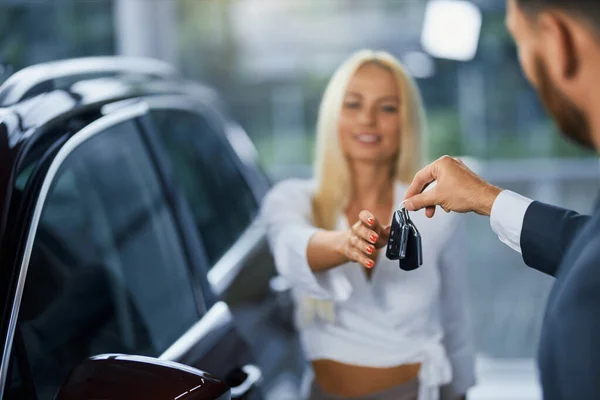 Mujer alegre tomando llaves de coche nuevo en el salón moderno —  Fotos de Stock