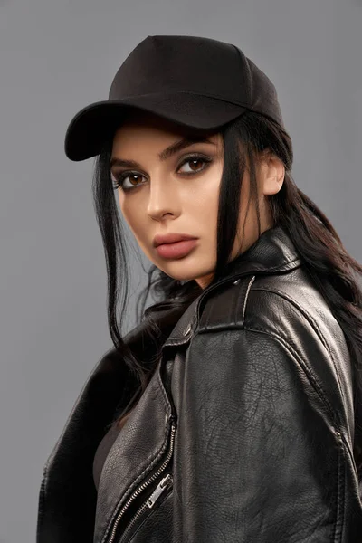 Attractive woman posing in studio in cap and leather jacket — Stock Photo, Image