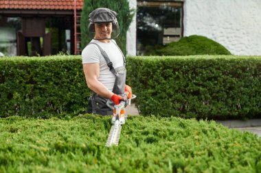 Caucasian man in uniform cutting bushes on backyard