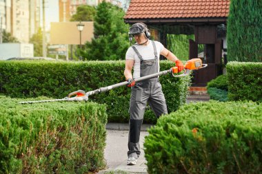 Man in uniform trimming bushes during warm sunny day