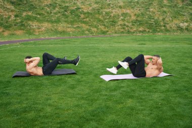 Two men with naked torso doing exercises for abs outdoors