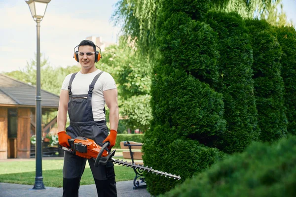Чоловік тримає електричний тример, стоячи в літньому саду — стокове фото