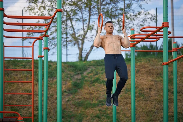 Strong bodybuilder training on gymnastic rings outdoors — Foto de Stock