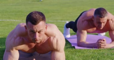 Sporty shirtless men standing in plank position on grass