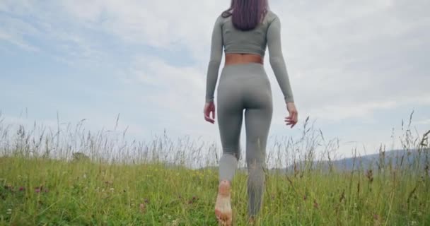 Vista posterior de la mujer en forma caminando con los pies descalzos sobre la hierba — Vídeos de Stock