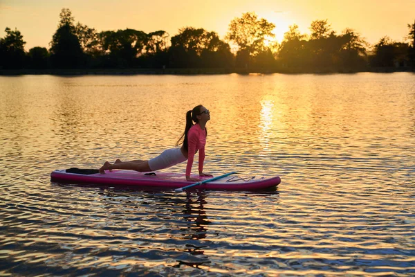 Junge athletische Frau praktiziert Sup Yoga bei Sonnenuntergang — Stockfoto