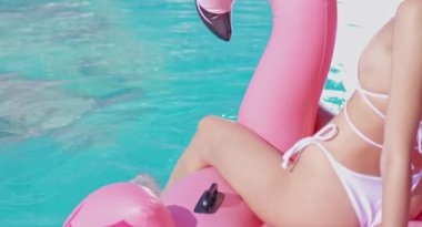 Havuzda şişme flamingo üzerinde oturan bikinili seksi kadın.