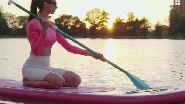 Sportliche Frau schwimmt auf Tretbrett auf Stadtsee — Stockvideo