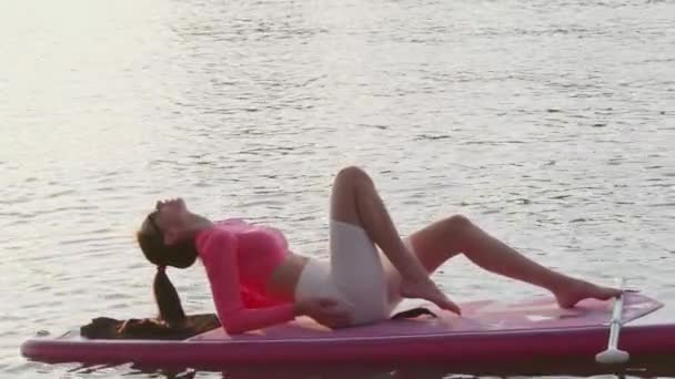 Вид збоку жінки, що плаває на дошці в вечірній час — стокове відео