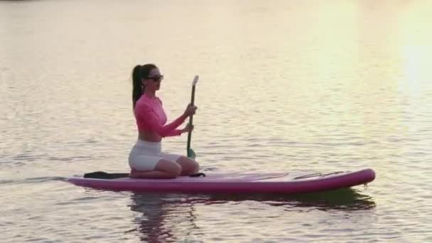 Mujer fitness practicando paddle boarding al atardecer — Vídeo de stock