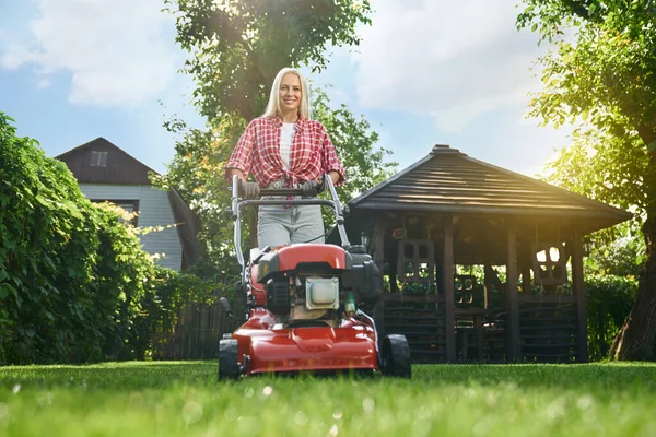 Wanita tersenyum menggunakan mesin pemotong rumput saat bekerja di kebun — Stok Foto