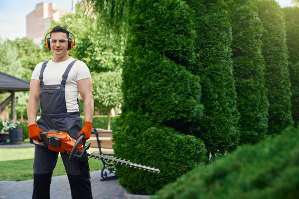 Mann som står i sommerhagen med elektrisk hekksaks – stockfoto