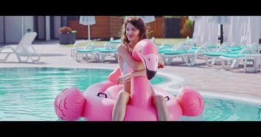 Bikinili esmer, şişme flamingoda havuzda yüzüyor.