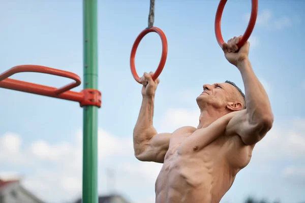 Muscular sin camisa hombre haciendo pull-ups en anillos gimnásticos — Foto de Stock