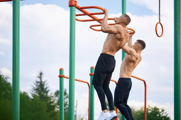 Два культуриста делают упражнения для оружия на спортивной площадке — стоковое фото