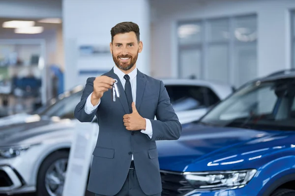 Empresario mostrando el pulgar hacia arriba y sosteniendo las llaves de un coche nuevo —  Fotos de Stock