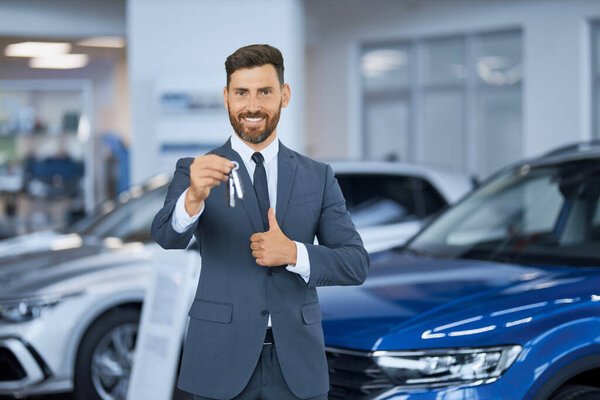 Businessman showing thumb up and holding keys from new car 