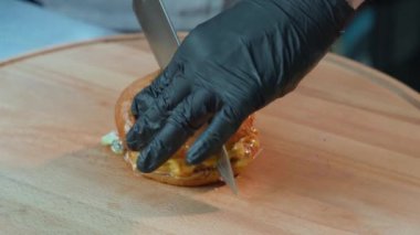 Ahşap tahtada bıçakla lezzetli bir burger kesen şef.