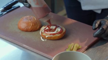 Eldivenli bir adam hamburger pişirirken çeşitli soslar sürüyor.