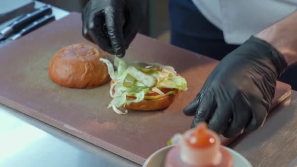 Chef-kok met behulp van verse groenten tijdens het maken van lekkere burger — Stockvideo