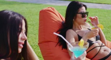 Bisiklet süren iki kadın kokteyl içip dışarıda güneşleniyor.