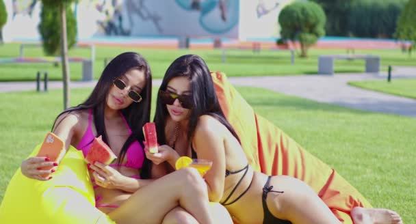 Bikinili iki kız dışarıda cep telefonuyla selfie çekiyor. — Stok video