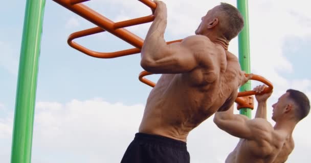 Two bodybuilders doing pull ups on sports ground — Stock Video