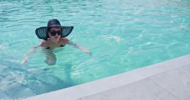 유행하는 모자를 쓰고 선글라스를 쓰고 비키니를 입고 수영장에서 수영하는 여자 — 비디오