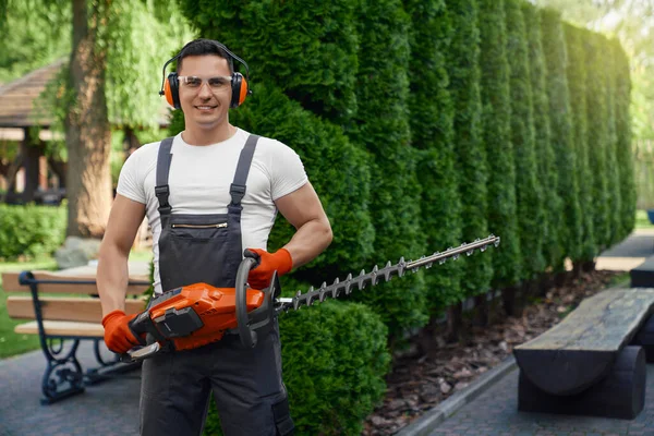 Man in overall holding hedge trimmer while posing at garden — Stok Foto