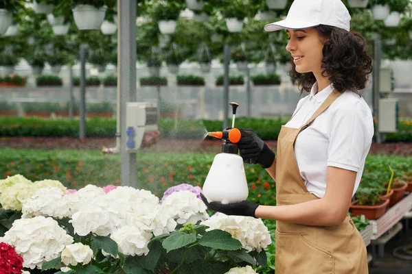 Young woman watering flowers in modern greenhouse. — Stock Photo, Image