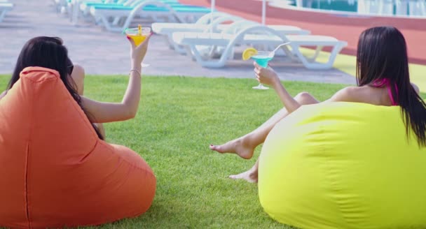 Zwei Frauen sitzen mit Getränken auf Sitzsäcken am Pool