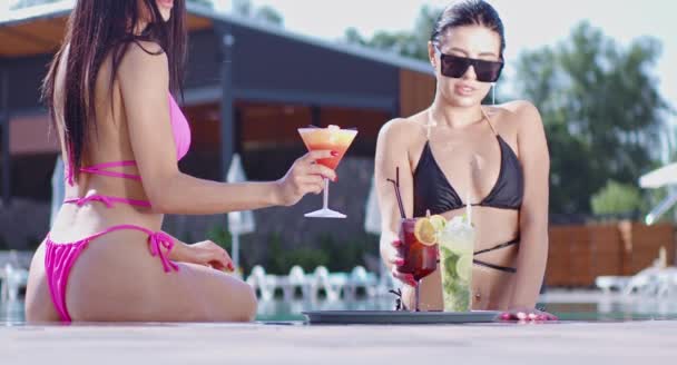 Two women in bikini drinking cocktails near swimming pool — Stock Video