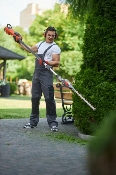 Uomo caucasico in uniforme sagomatura siepe con trimmer elettrico — Foto Stock