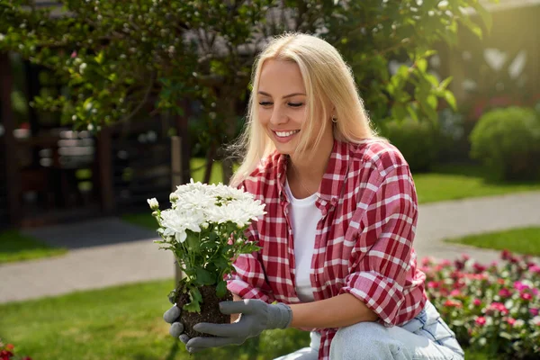 Glimlachende Kaukasische blonde verzorgen van bloemen in de tuin — Stockfoto