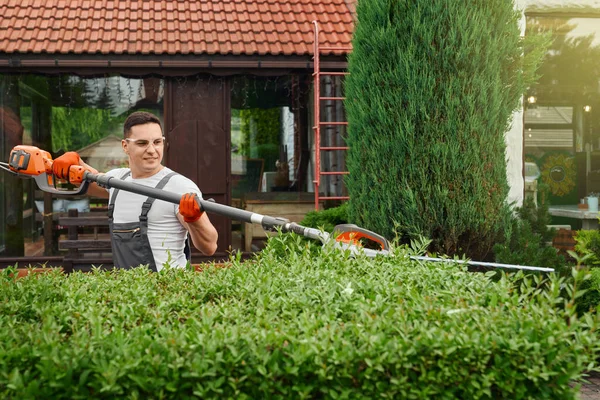 Mies käyttää sähkö pensasleikkuri työskennellessään puutarhassa — kuvapankkivalokuva